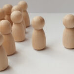 Group dynamics social interaction of wooden figurines minimalist studio photography neutral background close-up conceptual exploration