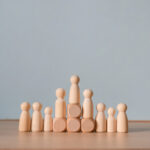 Wooden peg doll standing on block above group representing leadership hierarchy and career promotion achievement