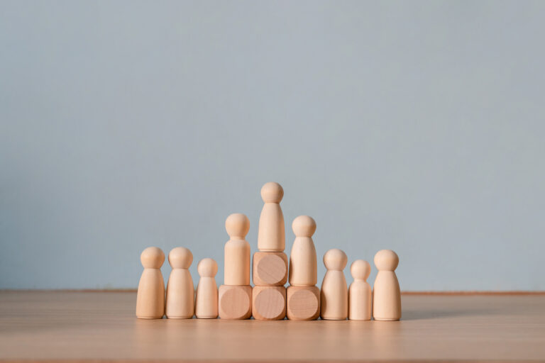 Wooden peg doll standing on block above group representing leadership hierarchy and career promotion achievement