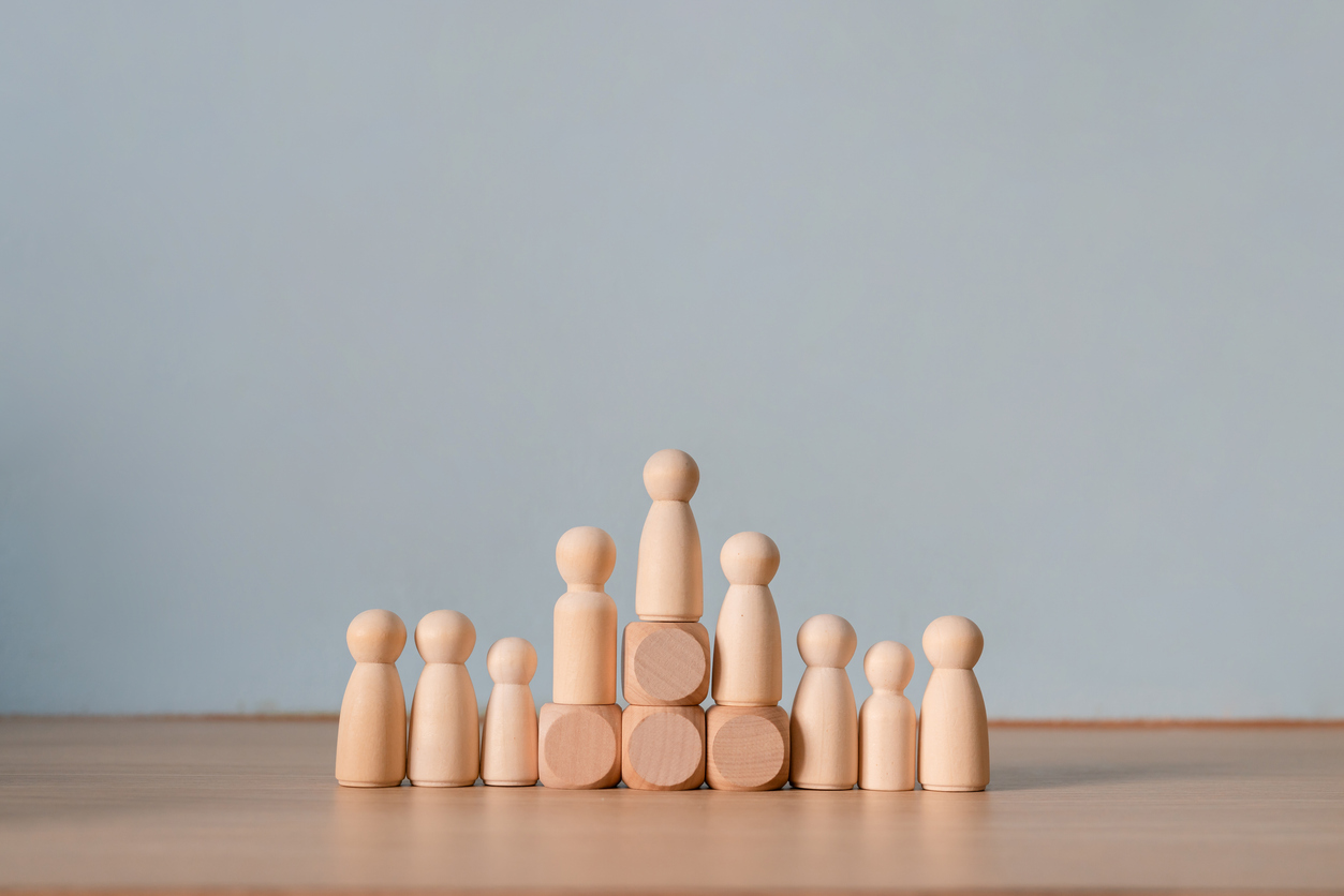 Wooden peg doll standing on block above group representing leadership hierarchy and career promotion achievement
